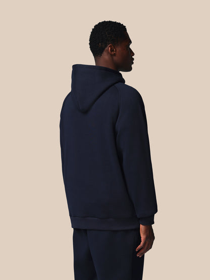 Person wearing a navy blue hoodie and pants on a beige background