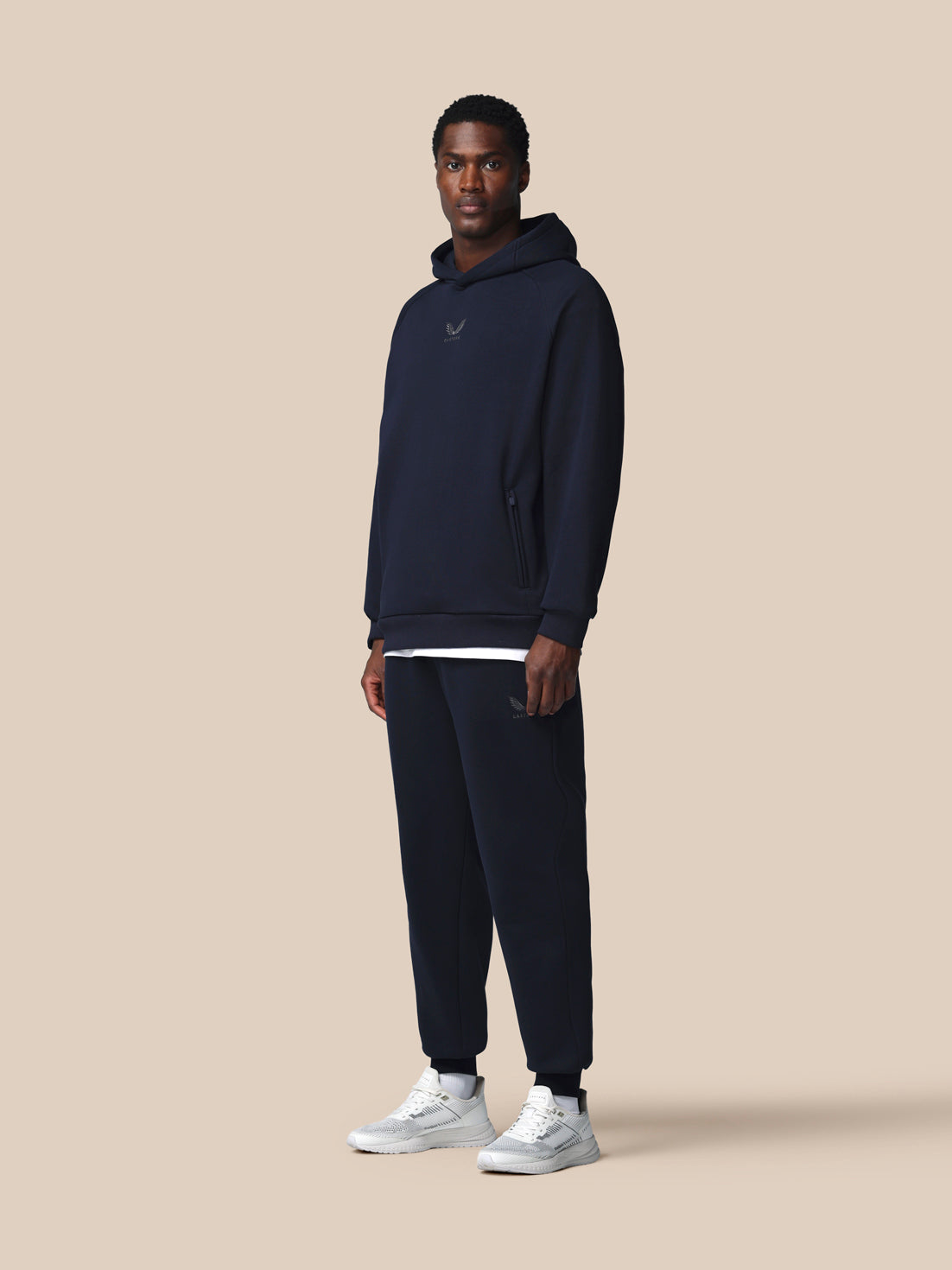 Man wearing a navy tracksuit with a logo on a beige background