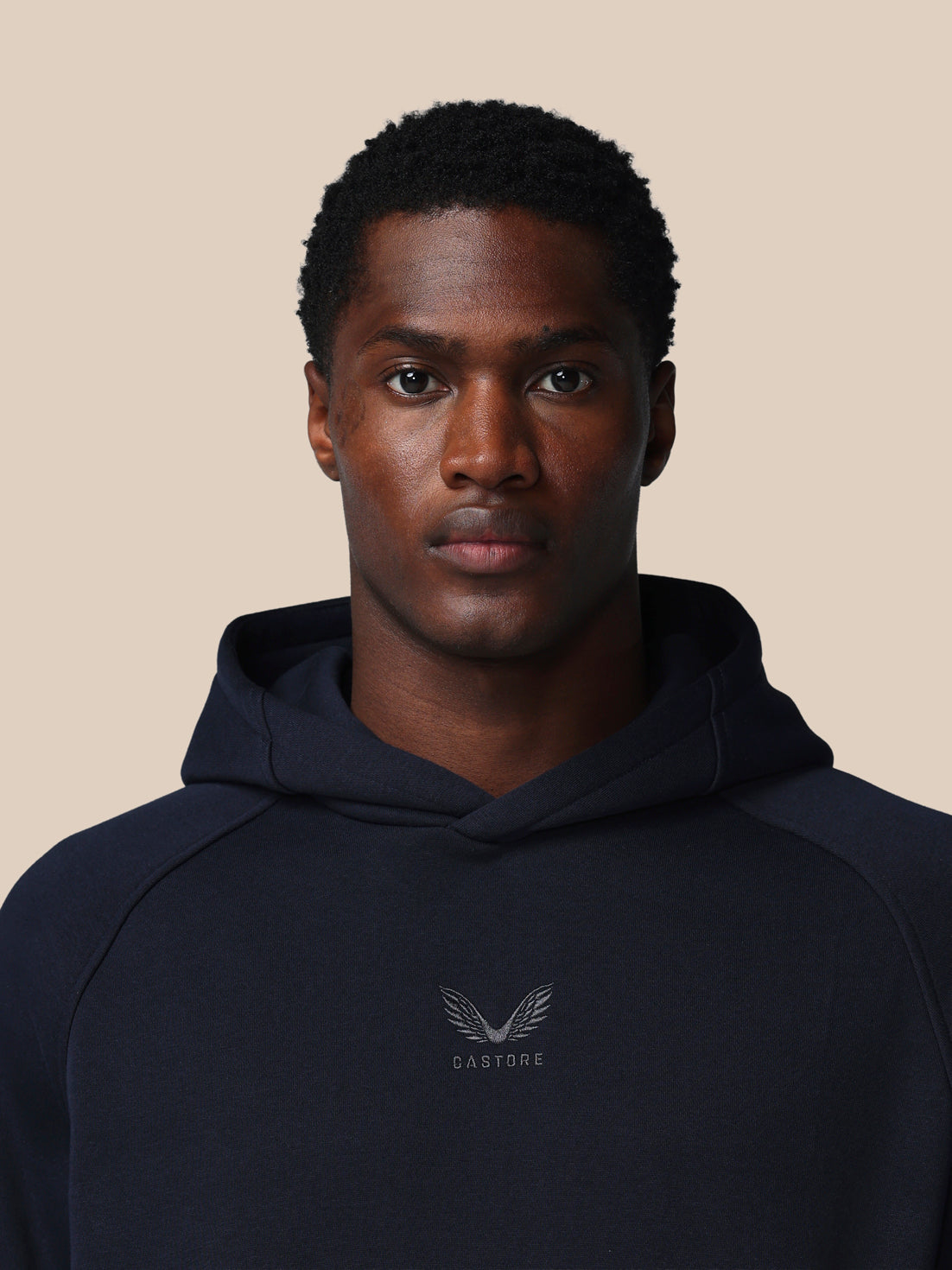 Man wearing a navy hoodie with a logo on a beige background