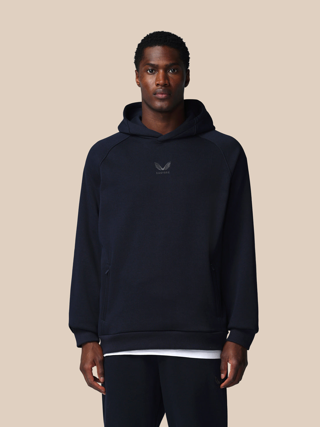 Man wearing a navy hoodie with a logo on a beige background