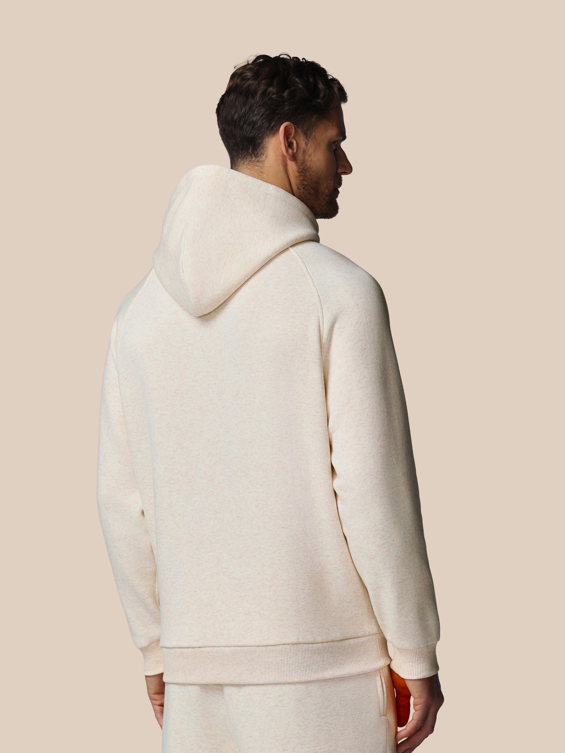 Man wearing a white hoodie and pants against a beige background