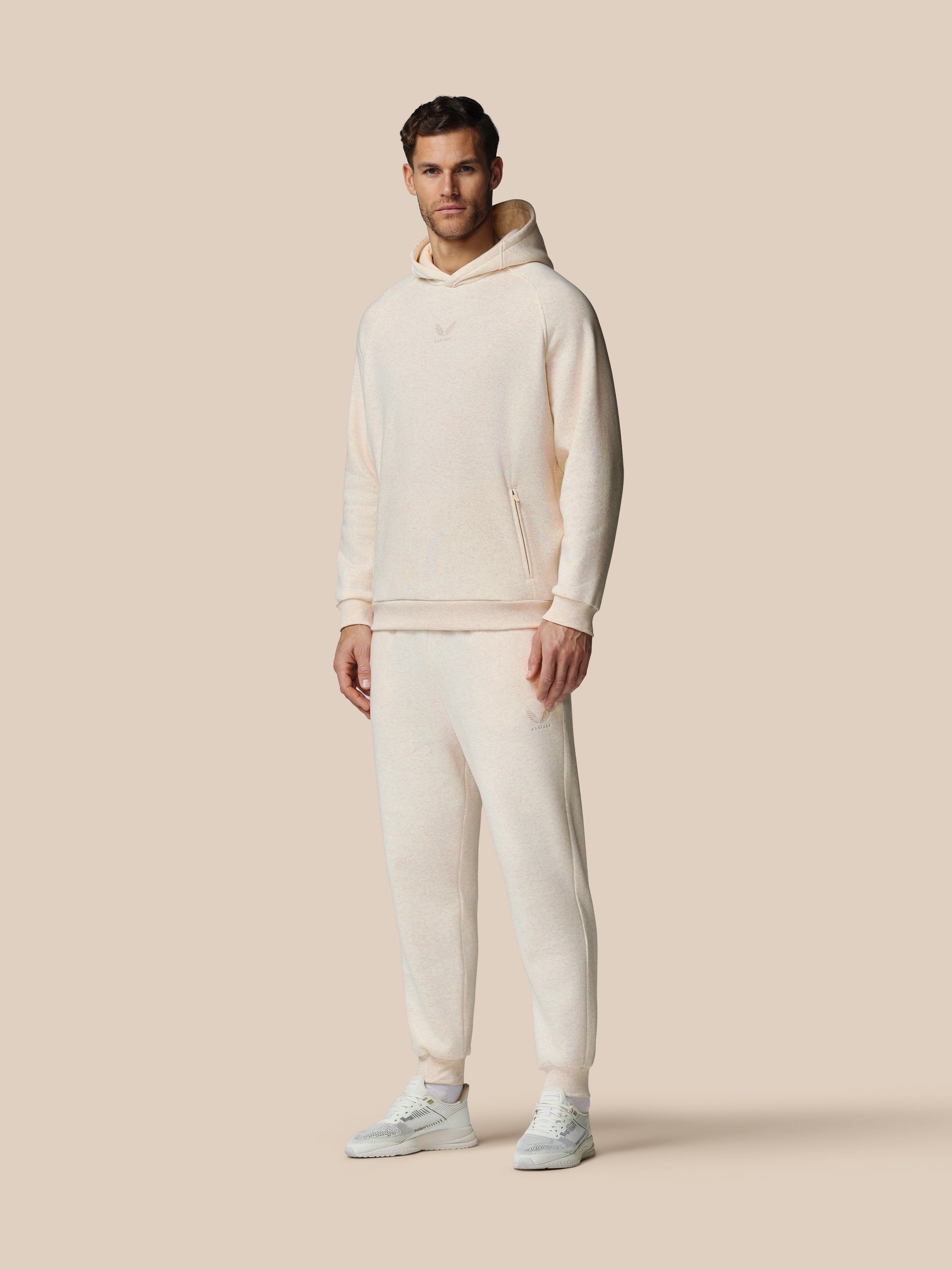 Man wearing a white hoodie and pants on a beige background