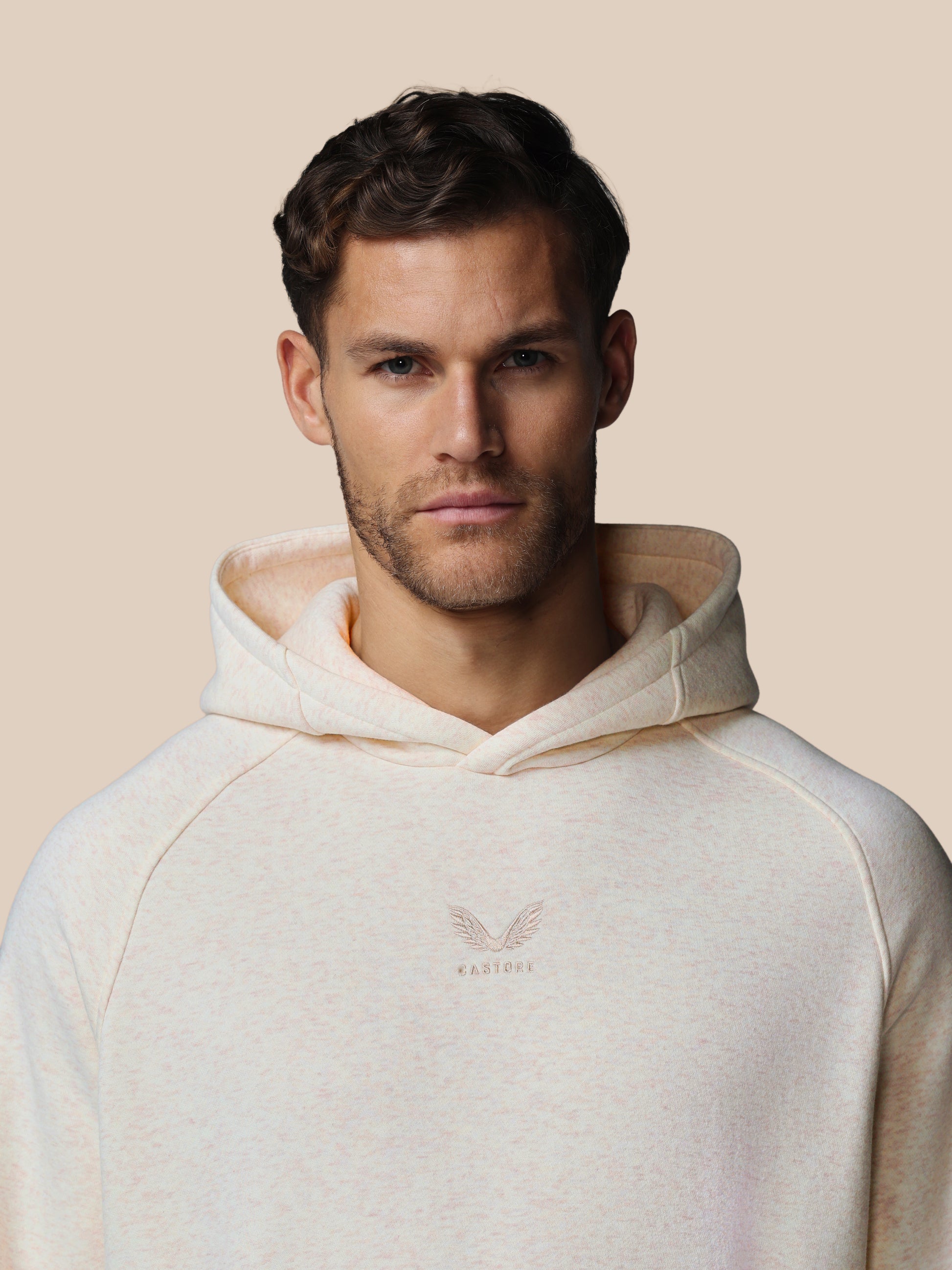 Man wearing a beige hoodie with a logo on a beige background
