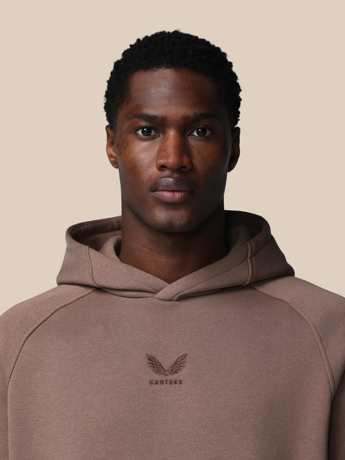 Man wearing a brown hoodie with a logo on a beige background