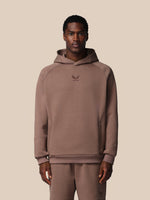 Man wearing a brown hoodie with a logo on a beige background