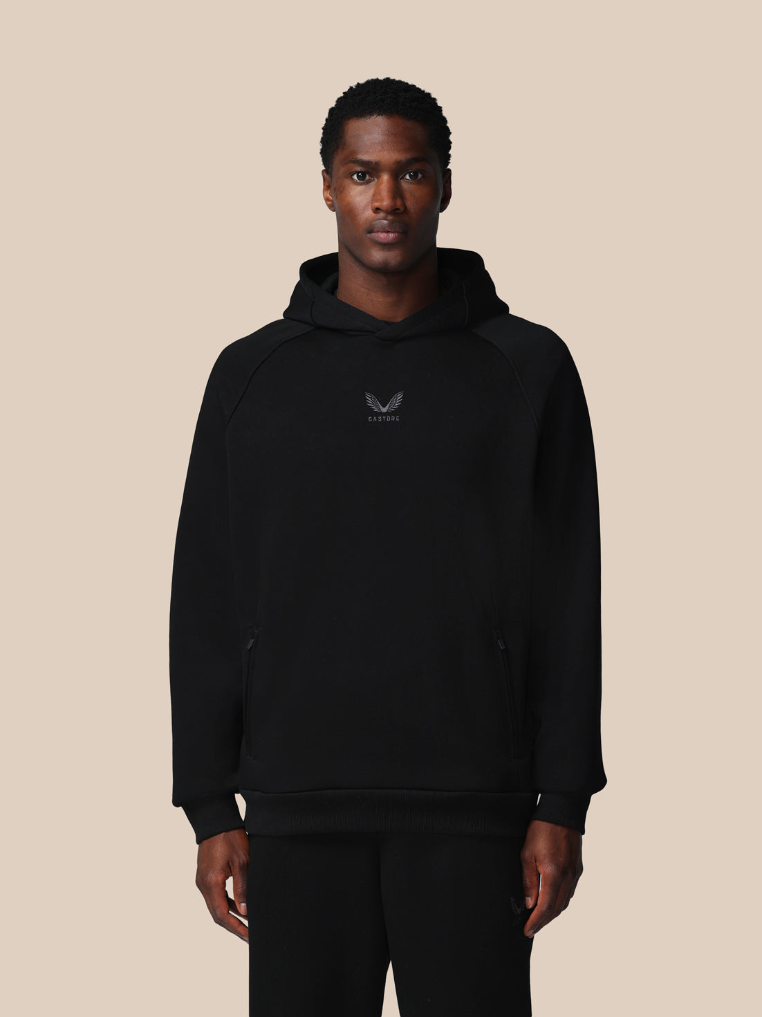 Man wearing a black hoodie with a logo on a beige background