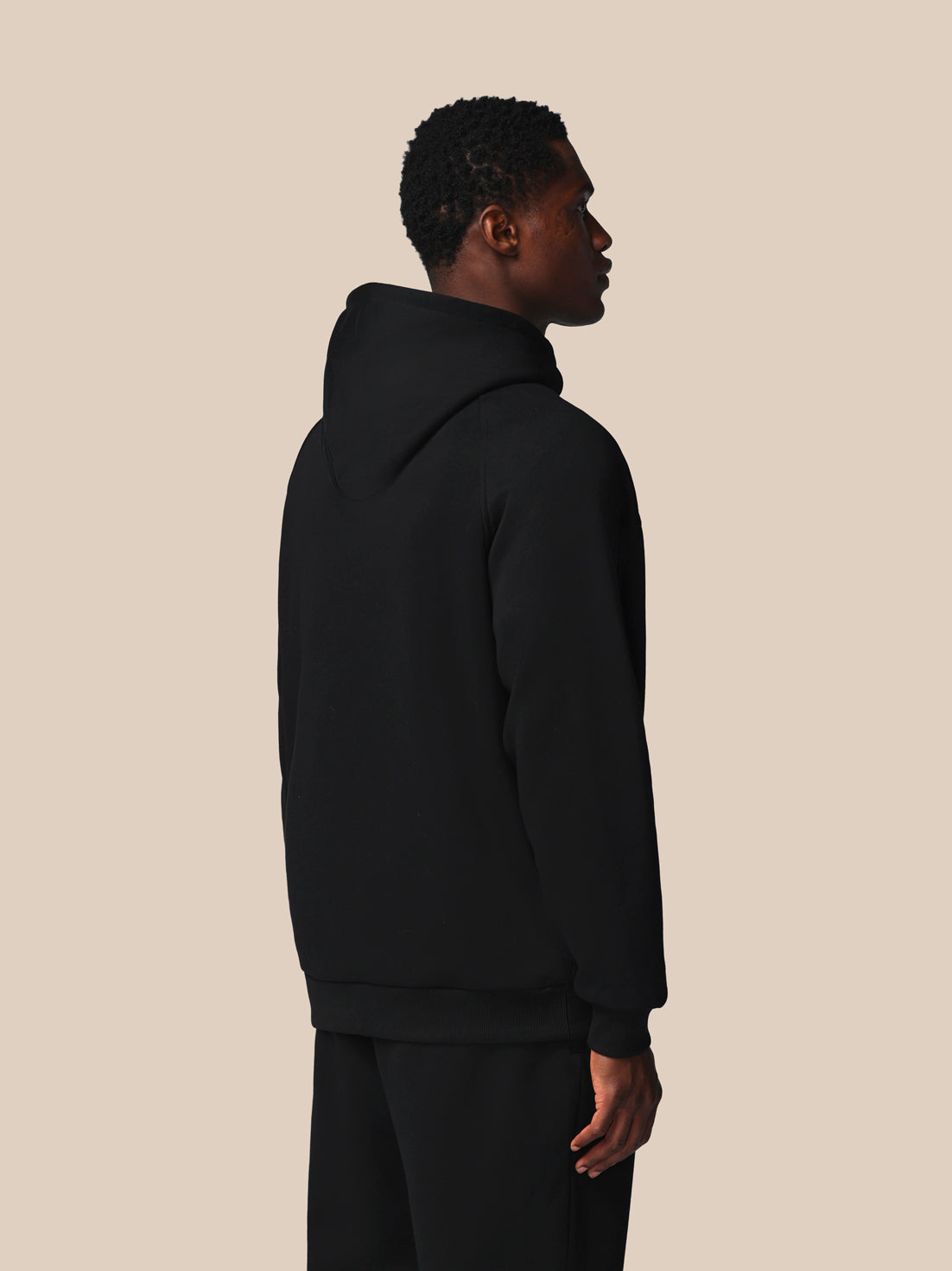 Person wearing a black hoodie and pants against a beige background