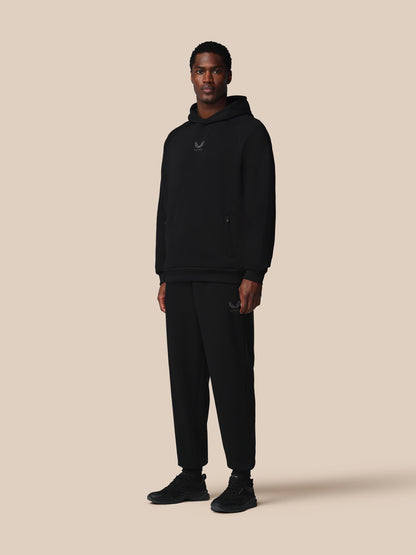 Man wearing a black hoodie and pants on a beige background