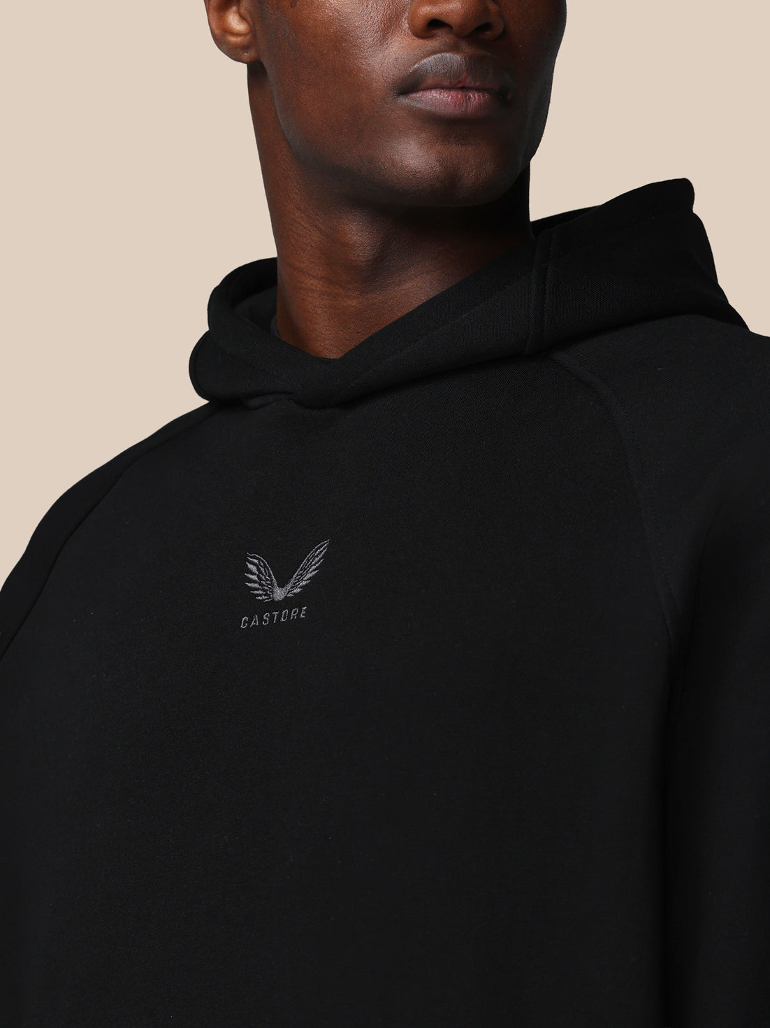 Person wearing a black hoodie with a logo on a beige background