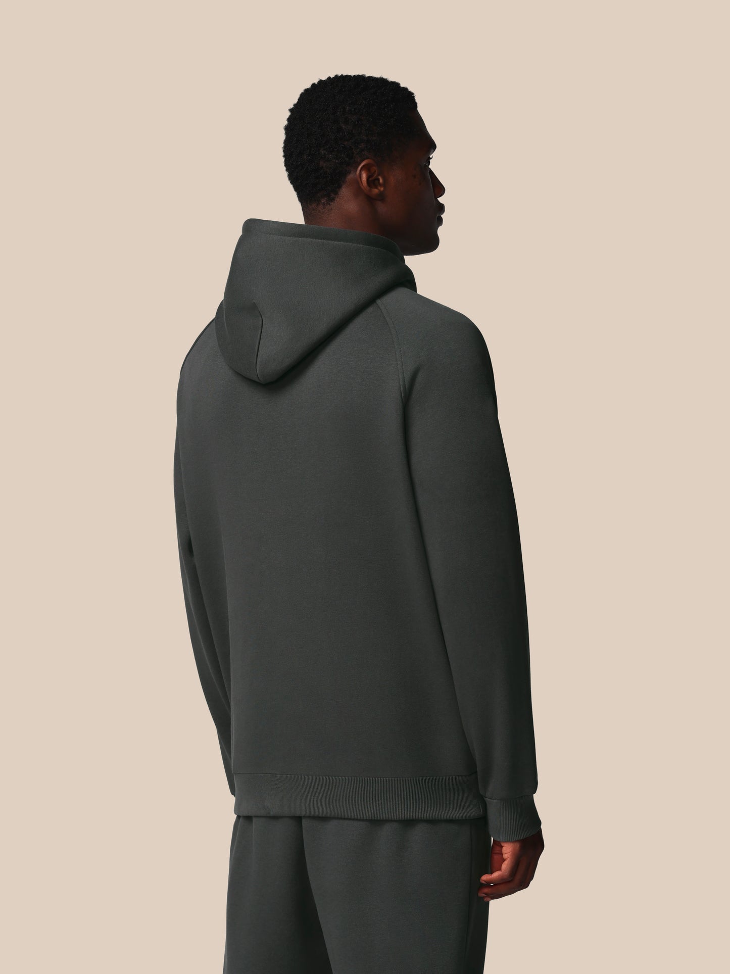 Person wearing a dark gray hoodie and pants on a beige background