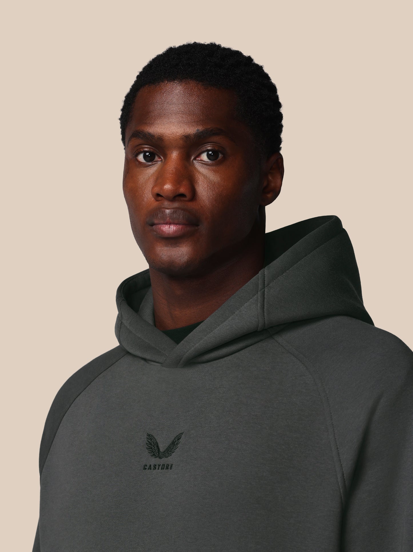Man wearing a dark gray hoodie with a logo on a beige background