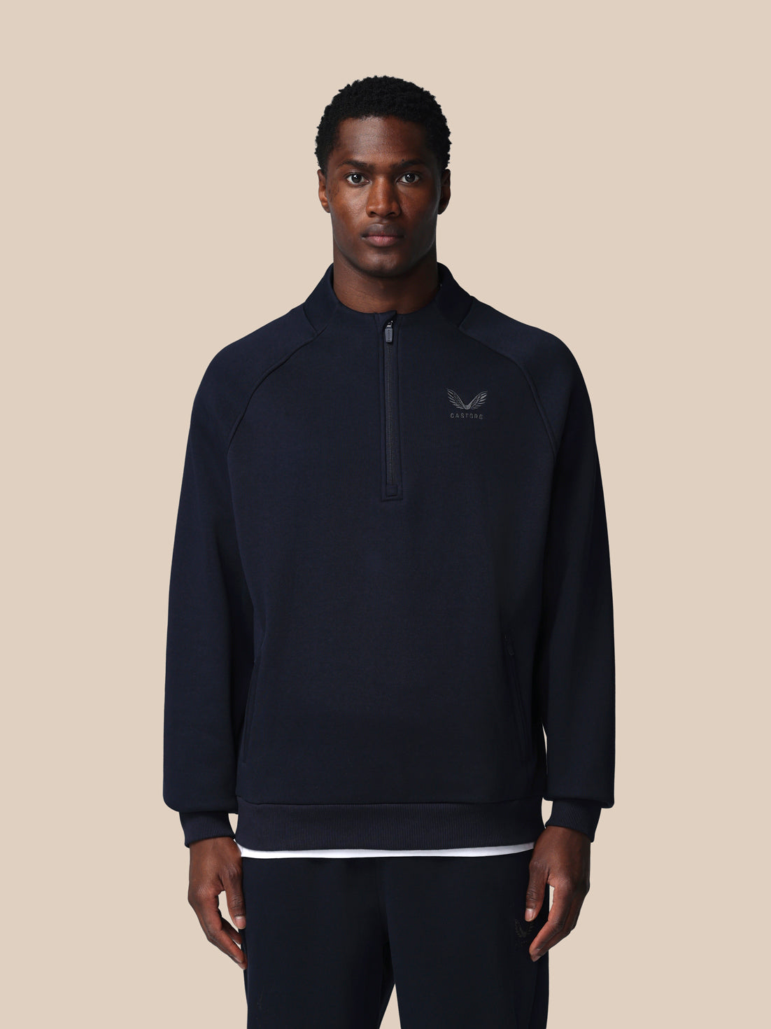 Man wearing a dark blue pullover with a logo on a beige background