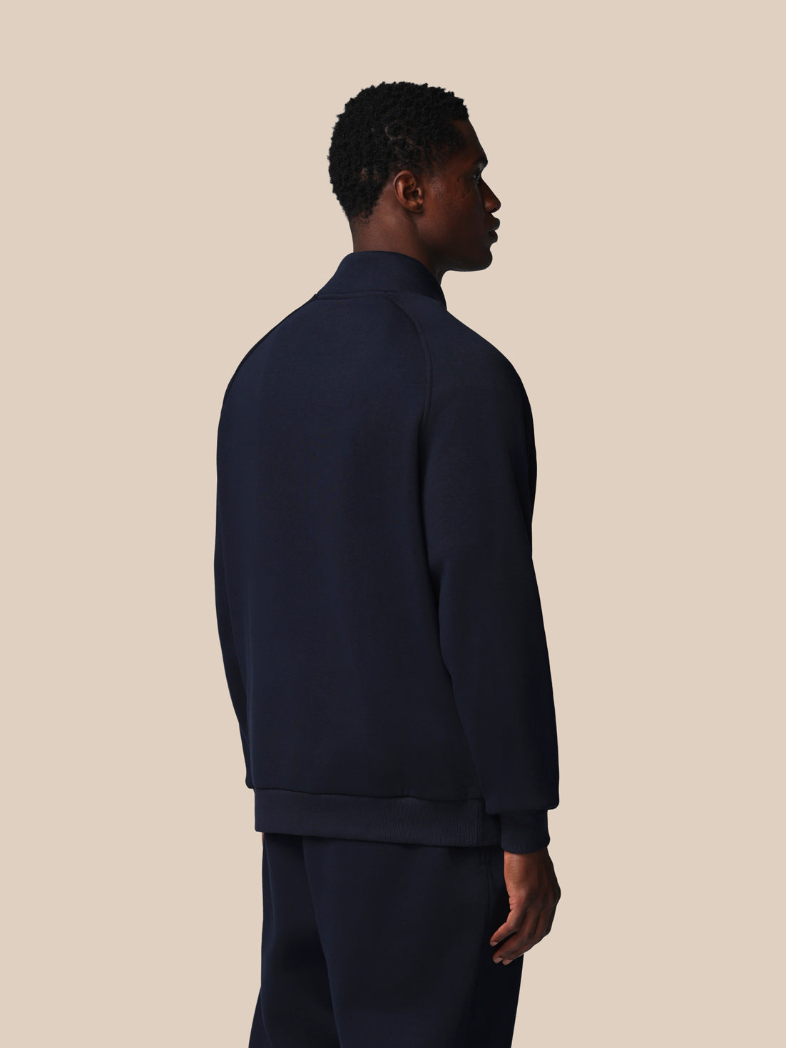 Person wearing a dark blue jacket and pants against a beige background
