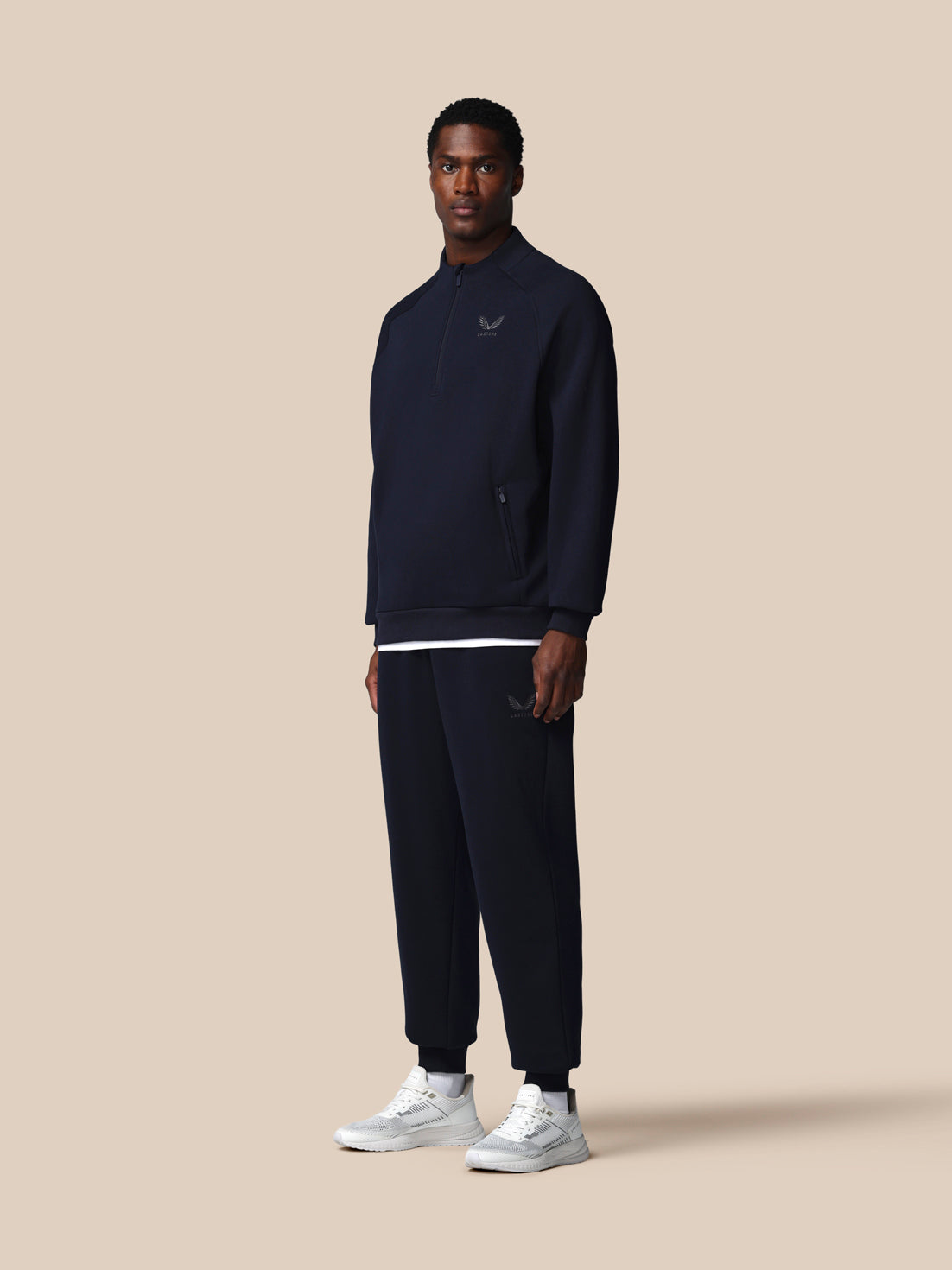 Man wearing a navy tracksuit with a logo on a beige background
