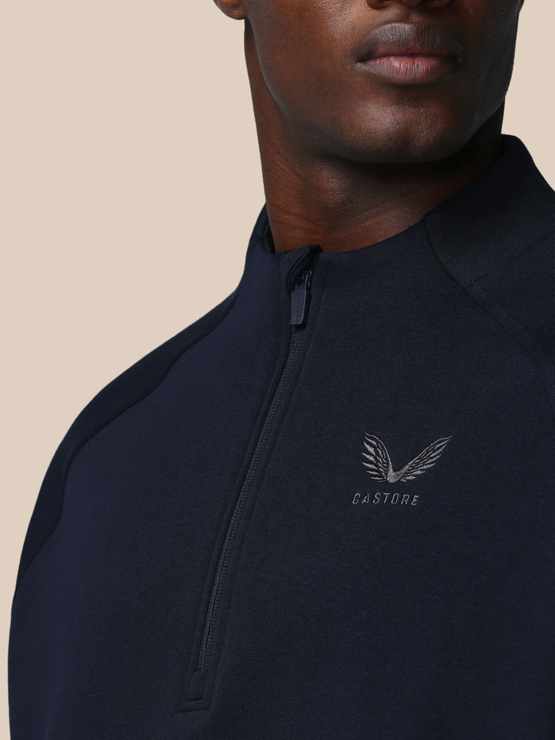 Person wearing a black quarter-zip sweatshirt with a brand logo on a beige background