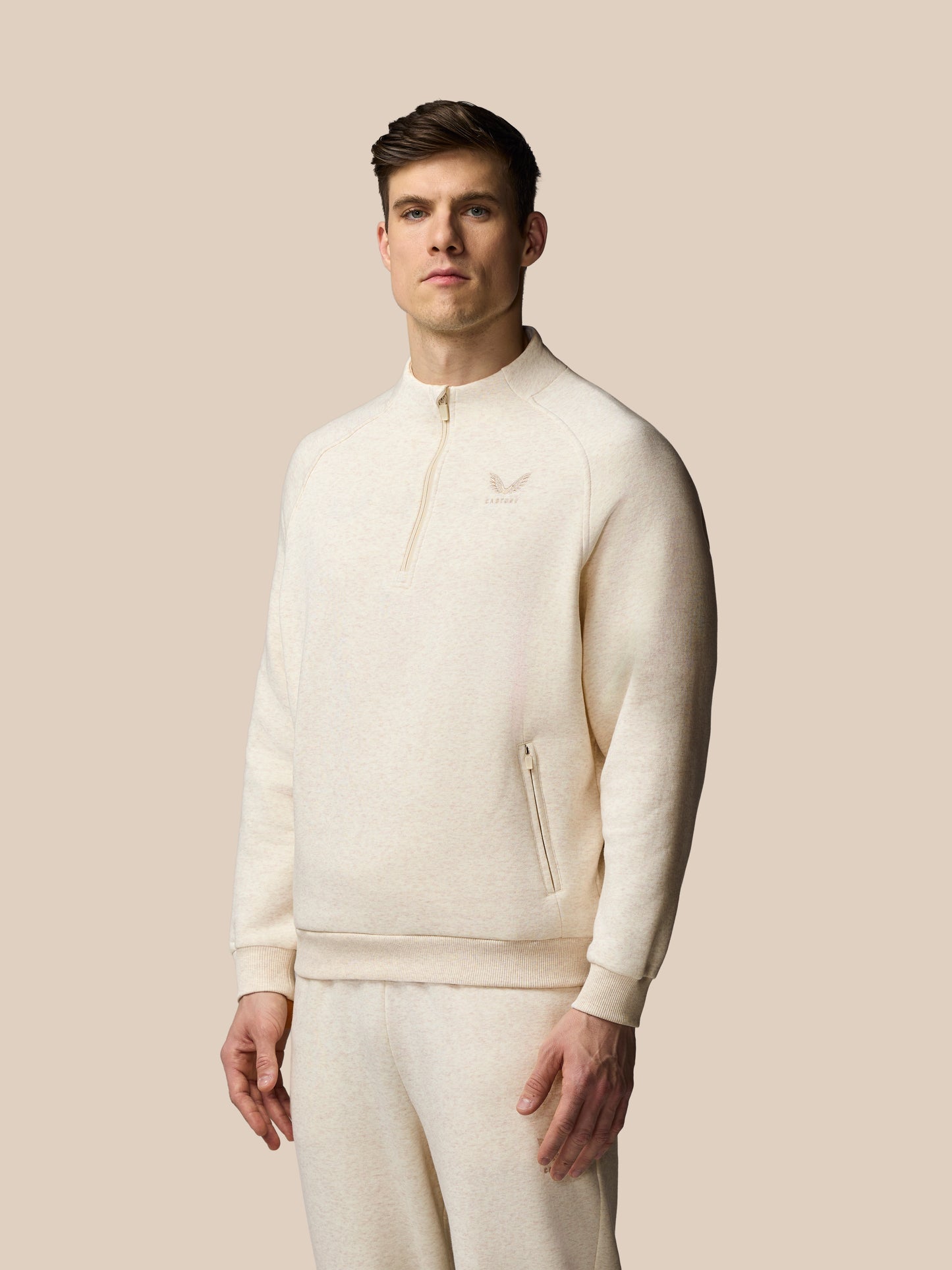 Man wearing a cream-colored outfit with a logo on a beige background