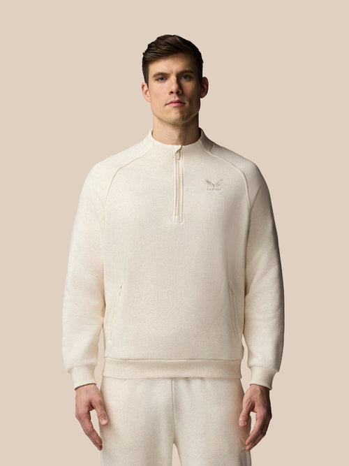 Man wearing a cream-colored tracksuit with a logo on a beige background