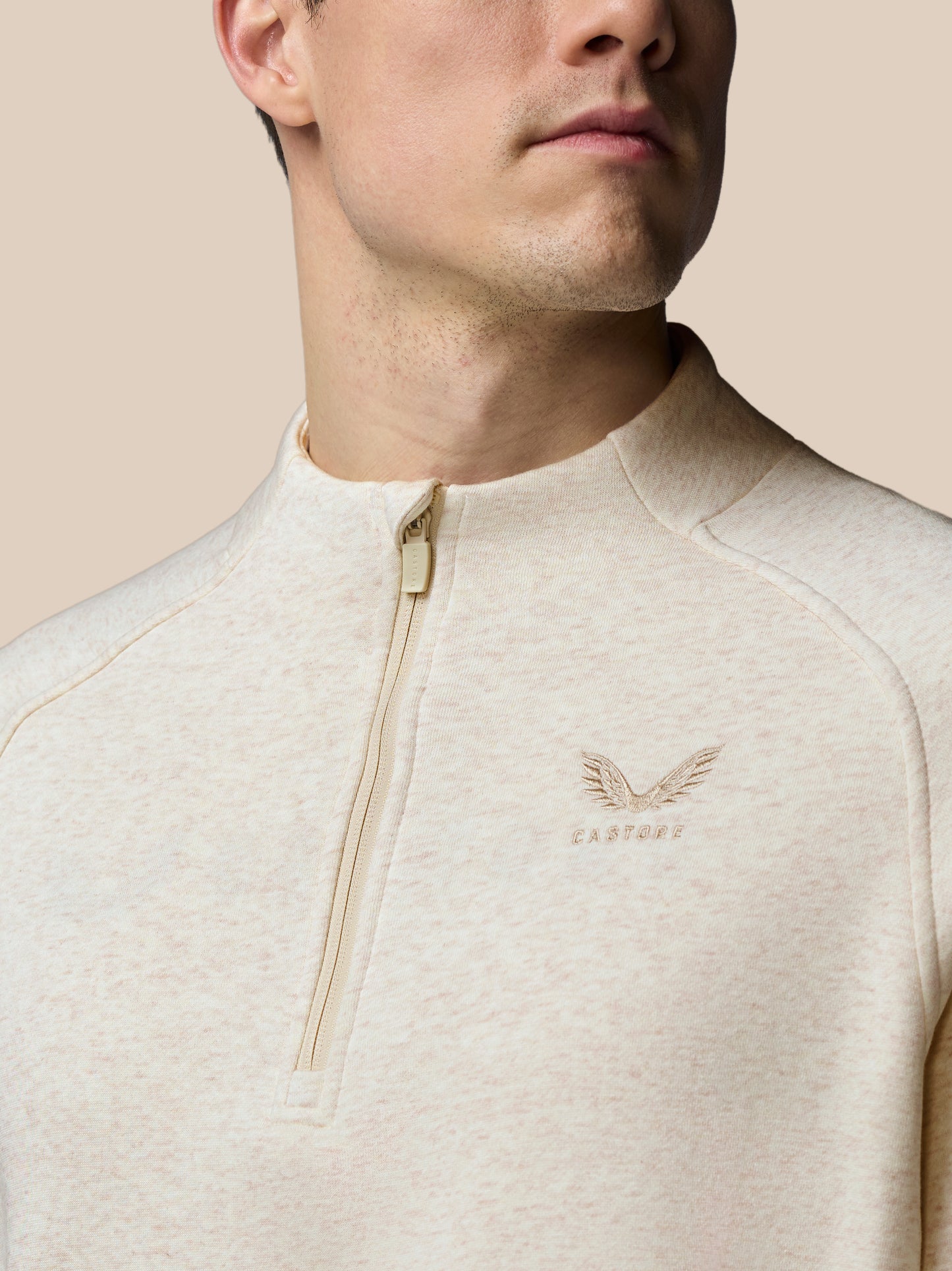 Close-up of a person wearing a beige athletic jacket with a brand logo on a beige background