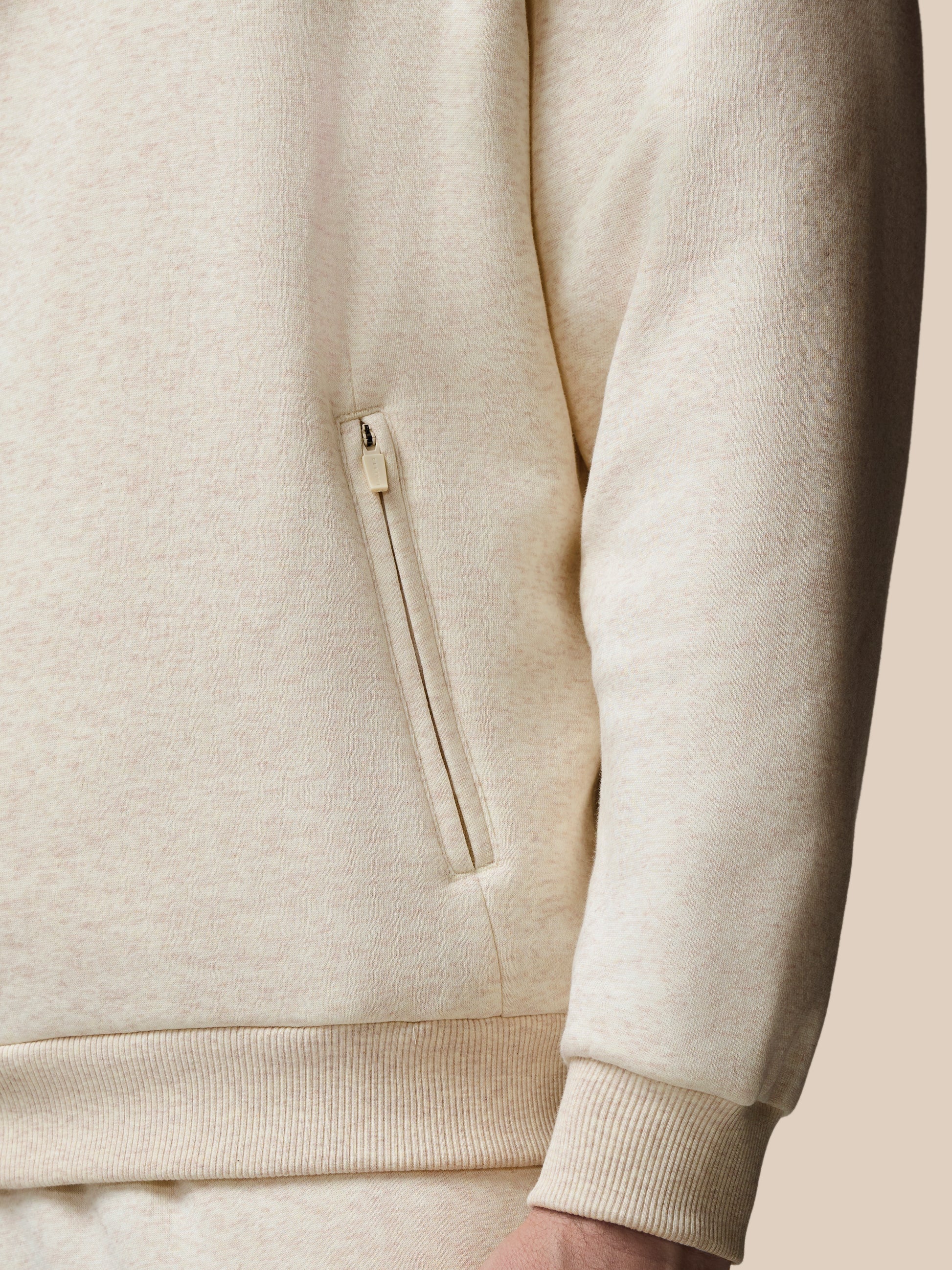 Close-up of a beige hoodie with a zipper pocket on a neutral background