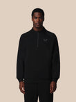 Person wearing a black zip-up sweatshirt with a logo on a beige background