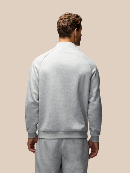 A man viewed from behind wearing a light gray heathered quarter-zip sweatshirt and matching sweatpants against a solid beige background.