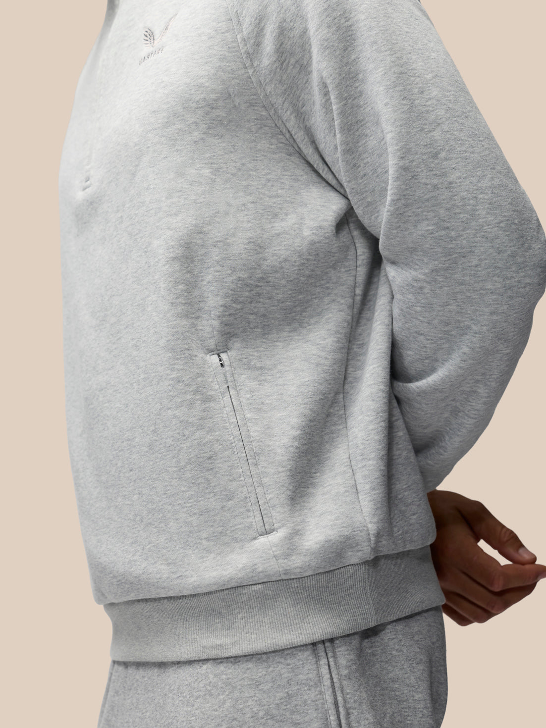 Close-up of a person wearing a light gray heather sweatshirt and matching sweatpants against a plain beige background.