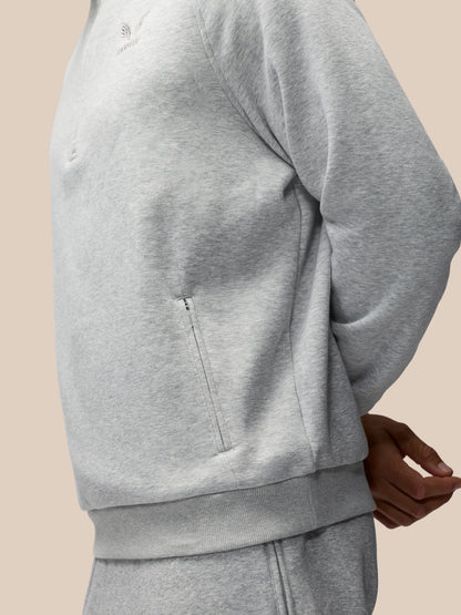 Close-up of a person wearing a light gray heather sweatshirt and matching sweatpants against a plain beige background.