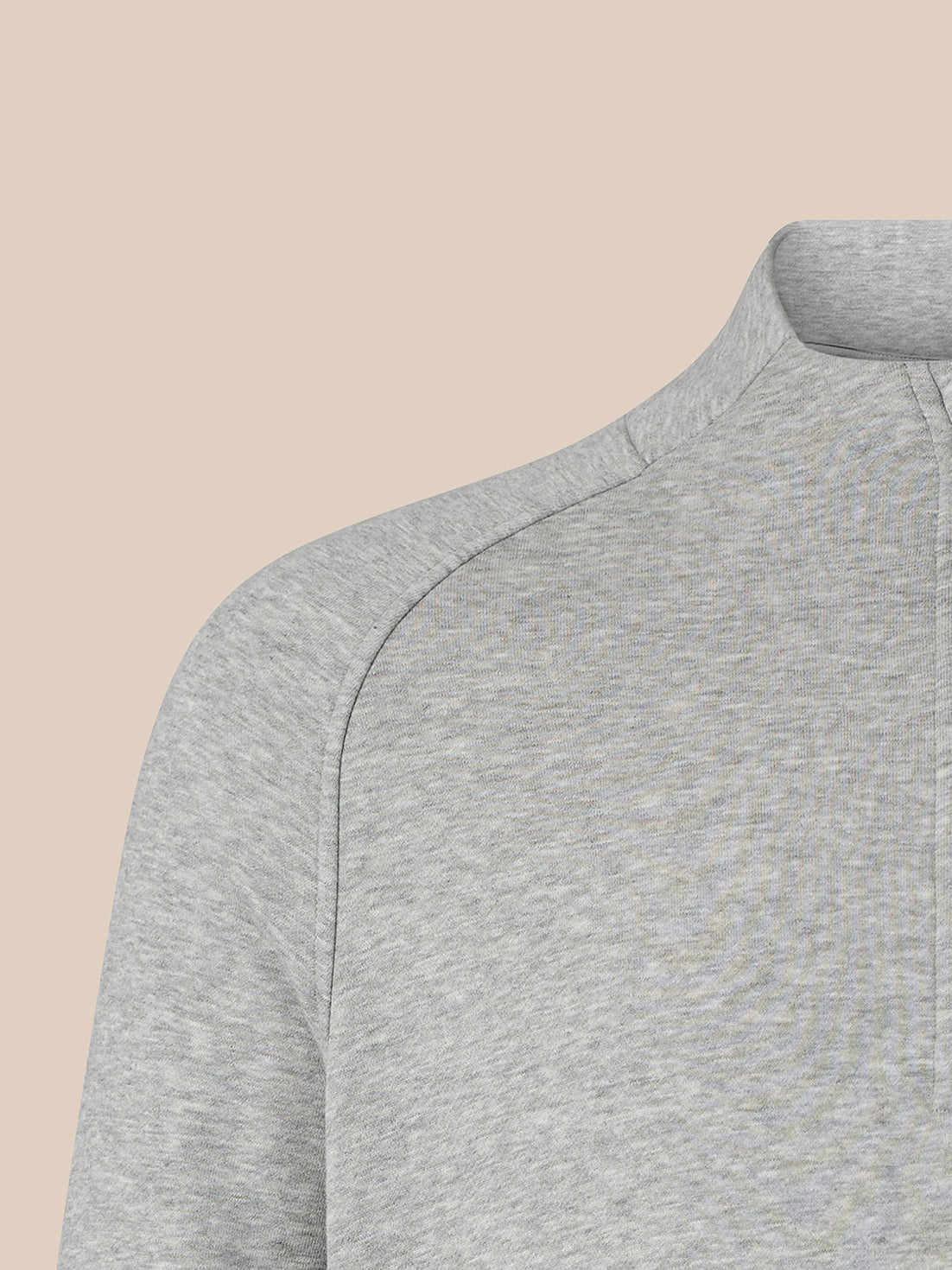 Close-up of a light gray heathered quarter-zip pullover sweater showing the shoulder seam and collar, set against a solid beige background.