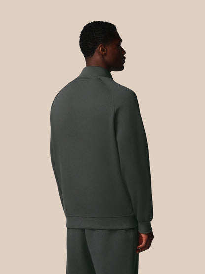 Person wearing a dark green tracksuit against a beige background