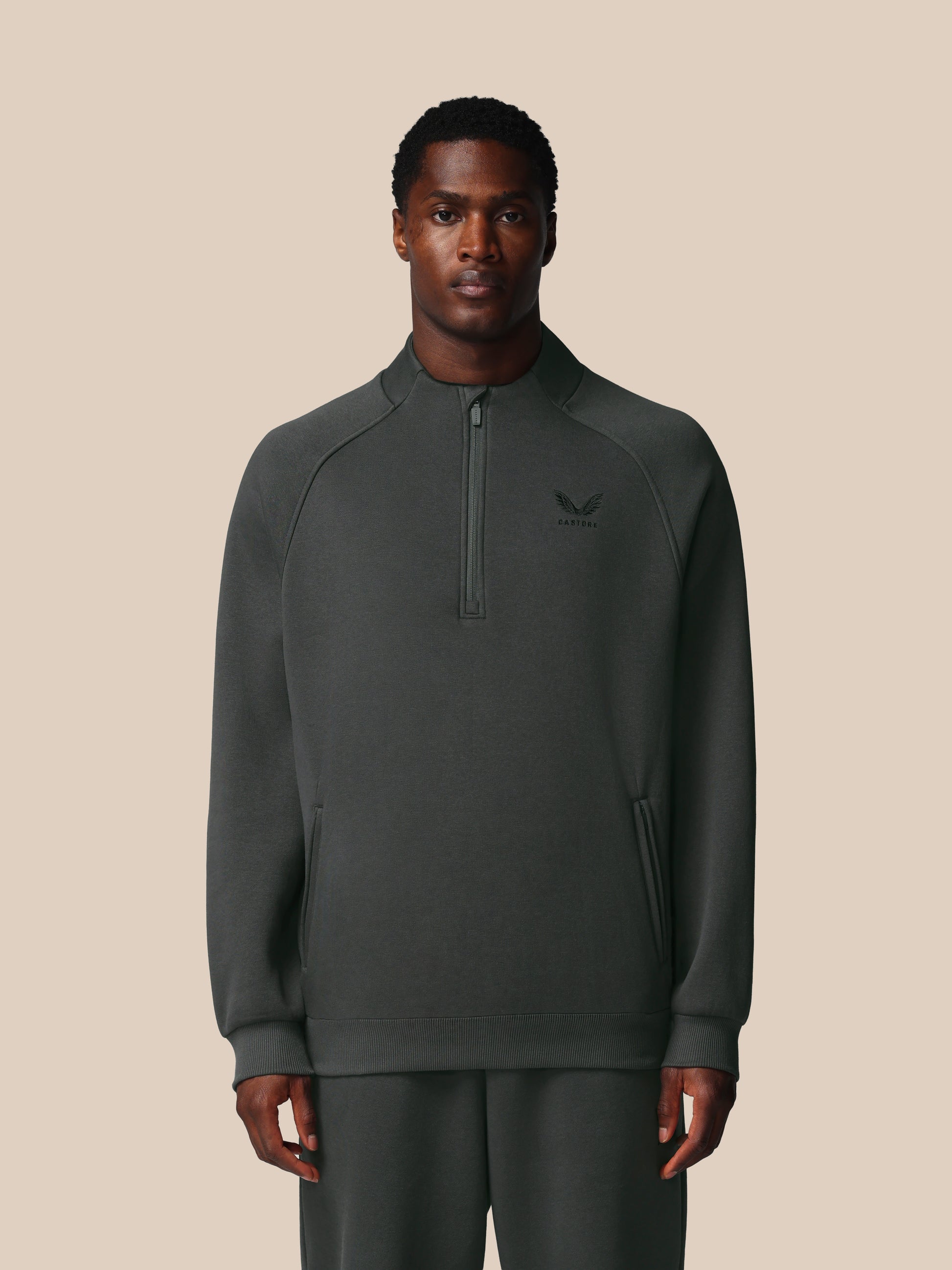 Man wearing a dark gray half-zip sweatshirt on a beige background