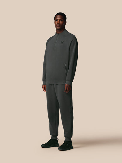 Man wearing a dark gray Castore tracksuit on a beige background