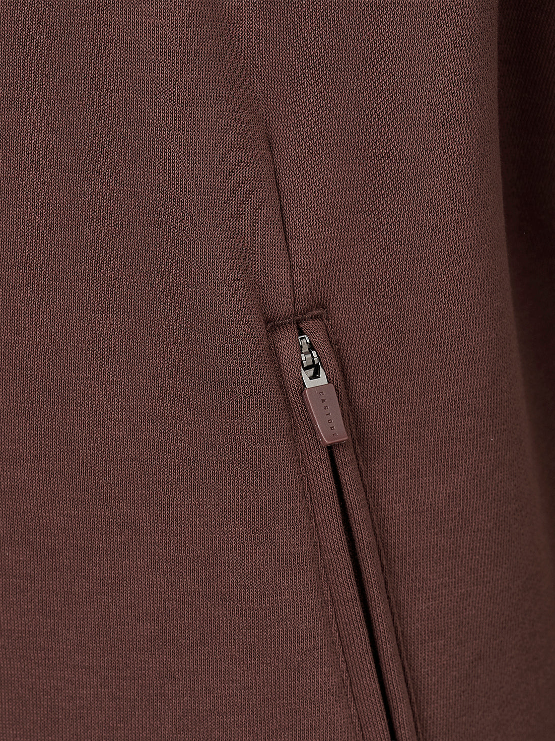 Close-up of a dark brown ribbed knit garment featuring a vertical zippered pocket with a matching brown pull tab.