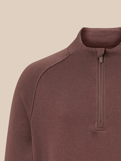 Close-up of a brown quarter-zip pullover sweater on a model, showing the collar, zipper, and shoulder seam against a solid beige background.