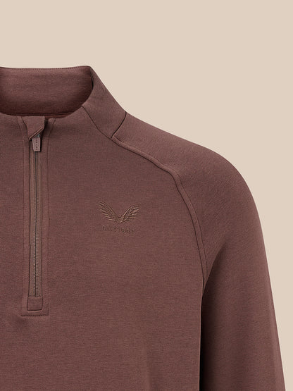 Close-up of a brown quarter-zip pullover sweater with a subtle embroidered winged logo on the left chest, set against a solid beige background.