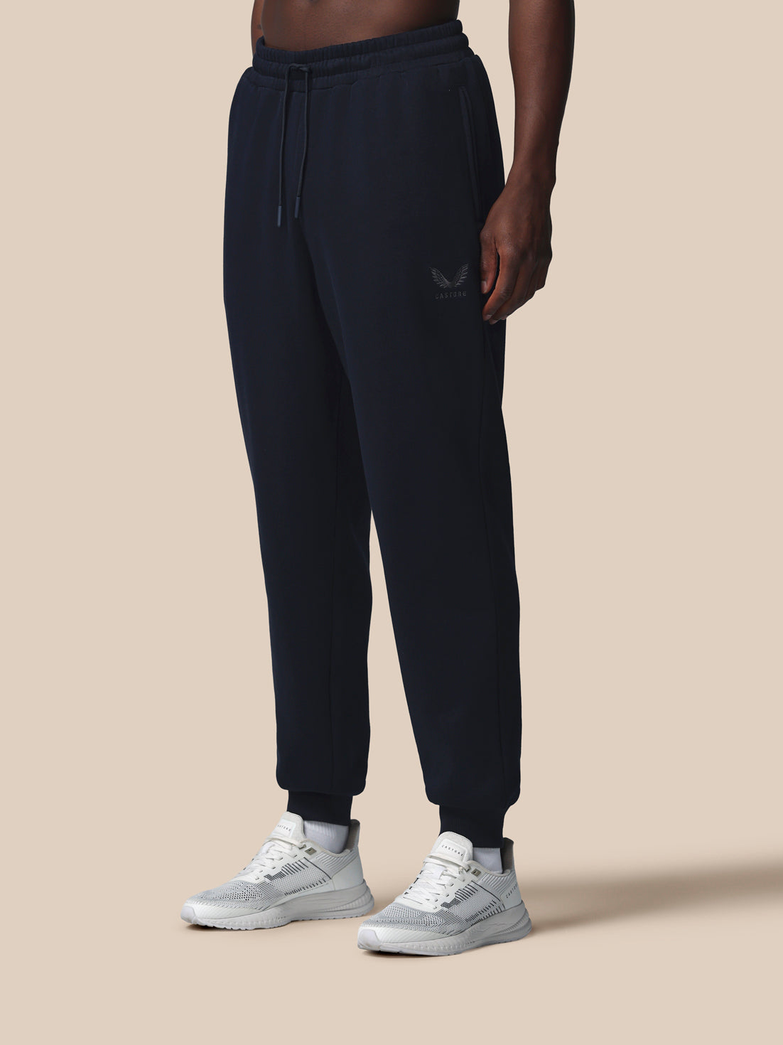 Person wearing black sweatpants and white sneakers on a beige background