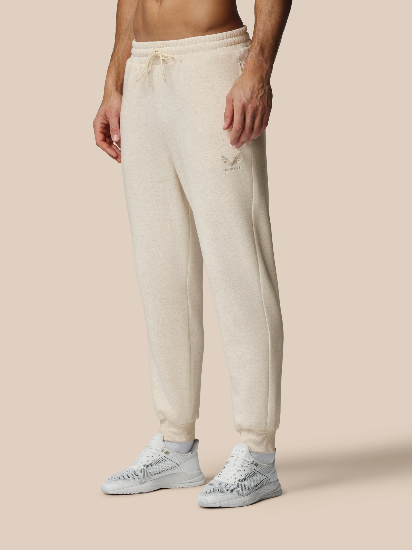 Person wearing beige sweatpants and white sneakers on a beige background