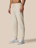 Person wearing beige sweatpants and white sneakers on a beige background