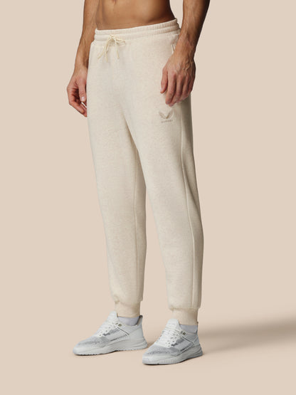 Person wearing beige sweatpants and white sneakers on a beige background