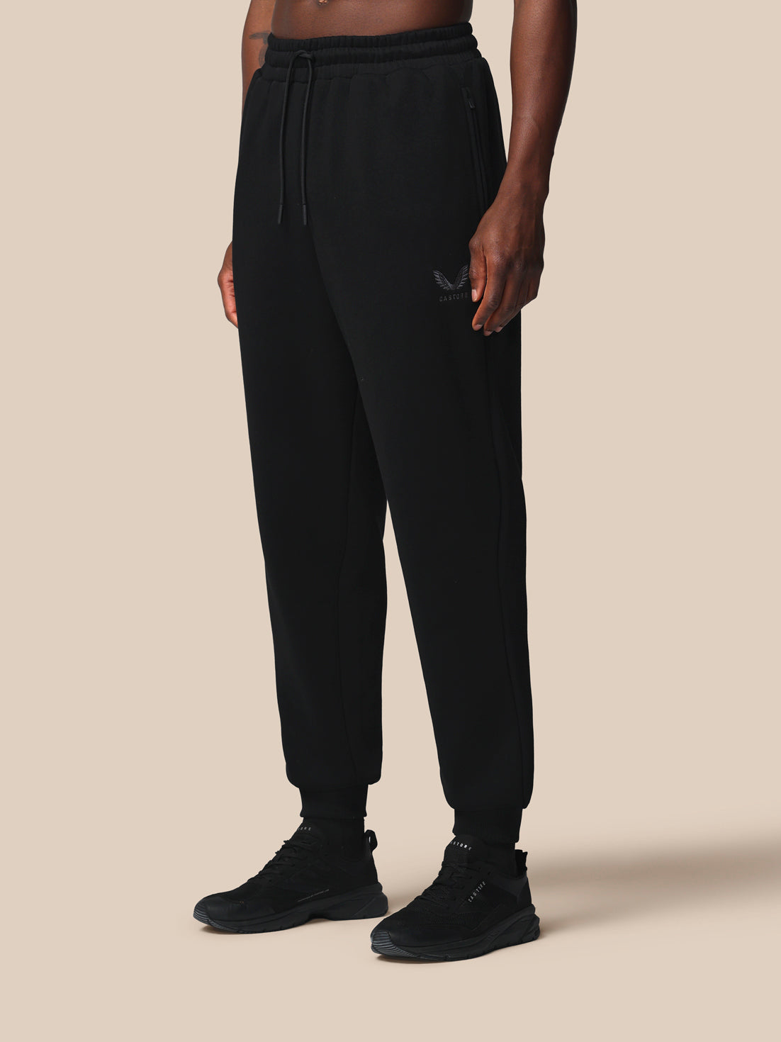 Person wearing black Castore sweatpants on a beige background