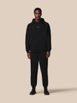 Person wearing a black hoodie and pants on a beige background