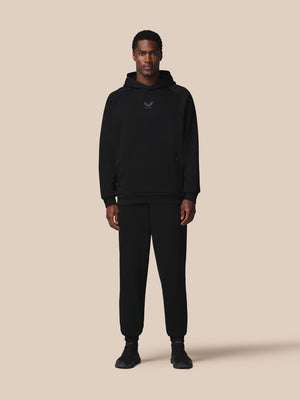 Person wearing a black hoodie and pants on a beige background