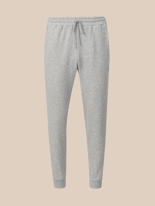 Light gray heather jogger sweatpants with an elastic waistband, drawstring, and ribbed ankle cuffs, shown against a solid beige background.