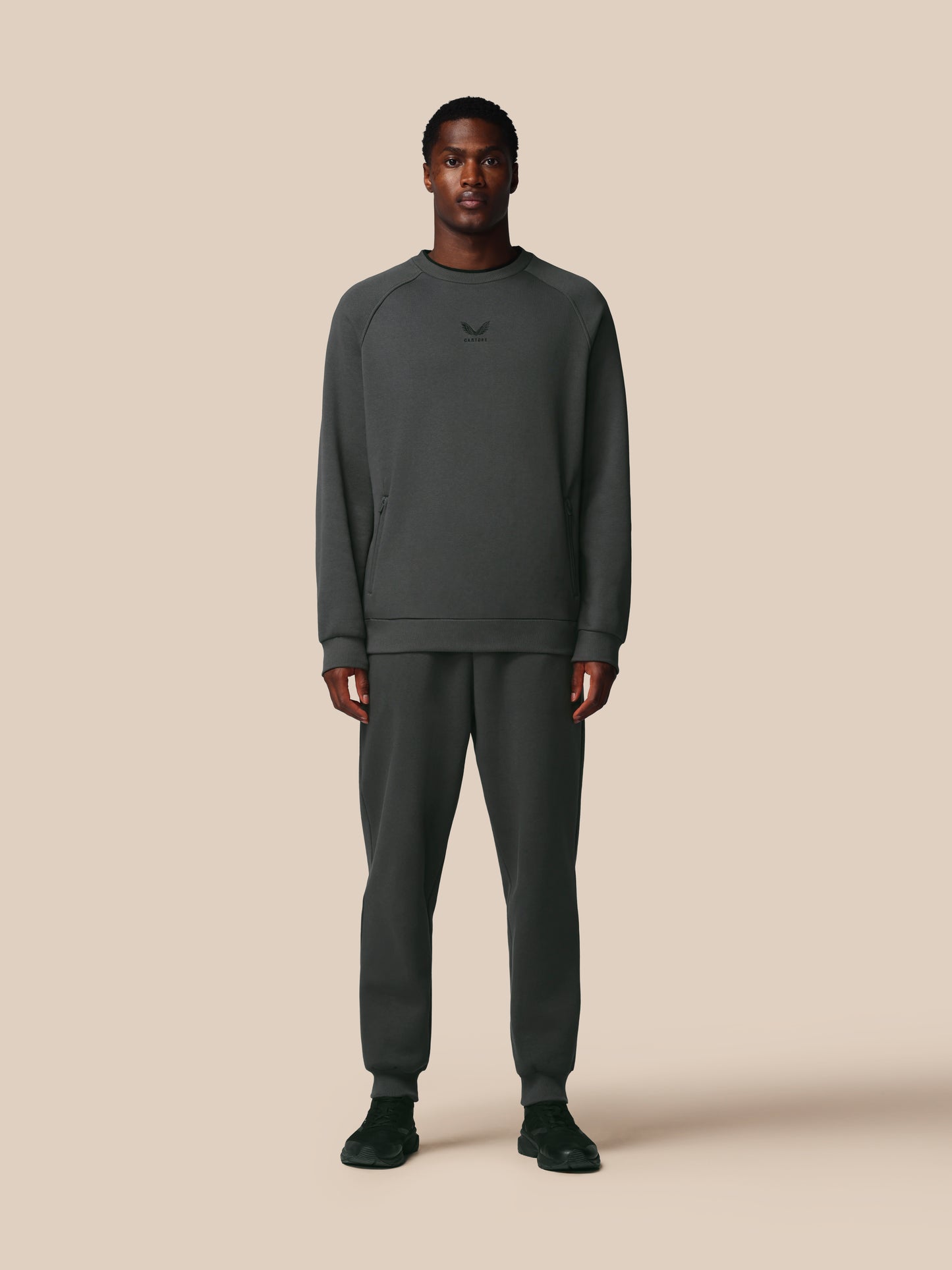 Man wearing a dark gray sweatshirt and pants on a beige background