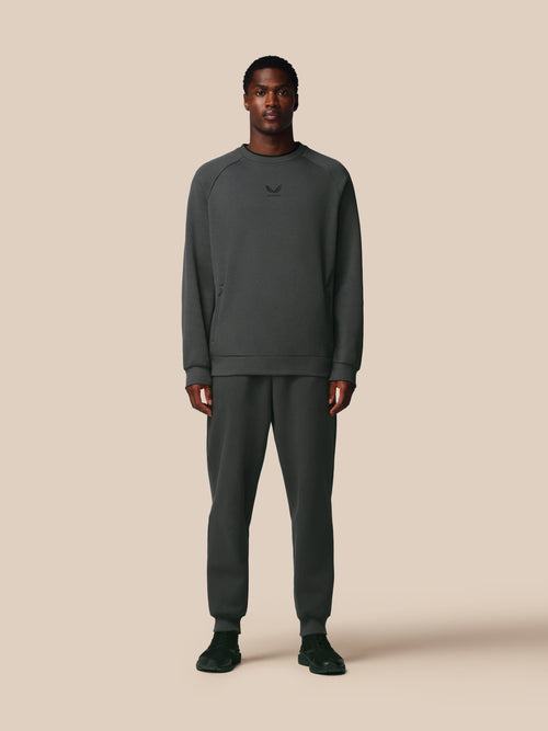 Man wearing a dark gray sweatshirt and pants on a beige background