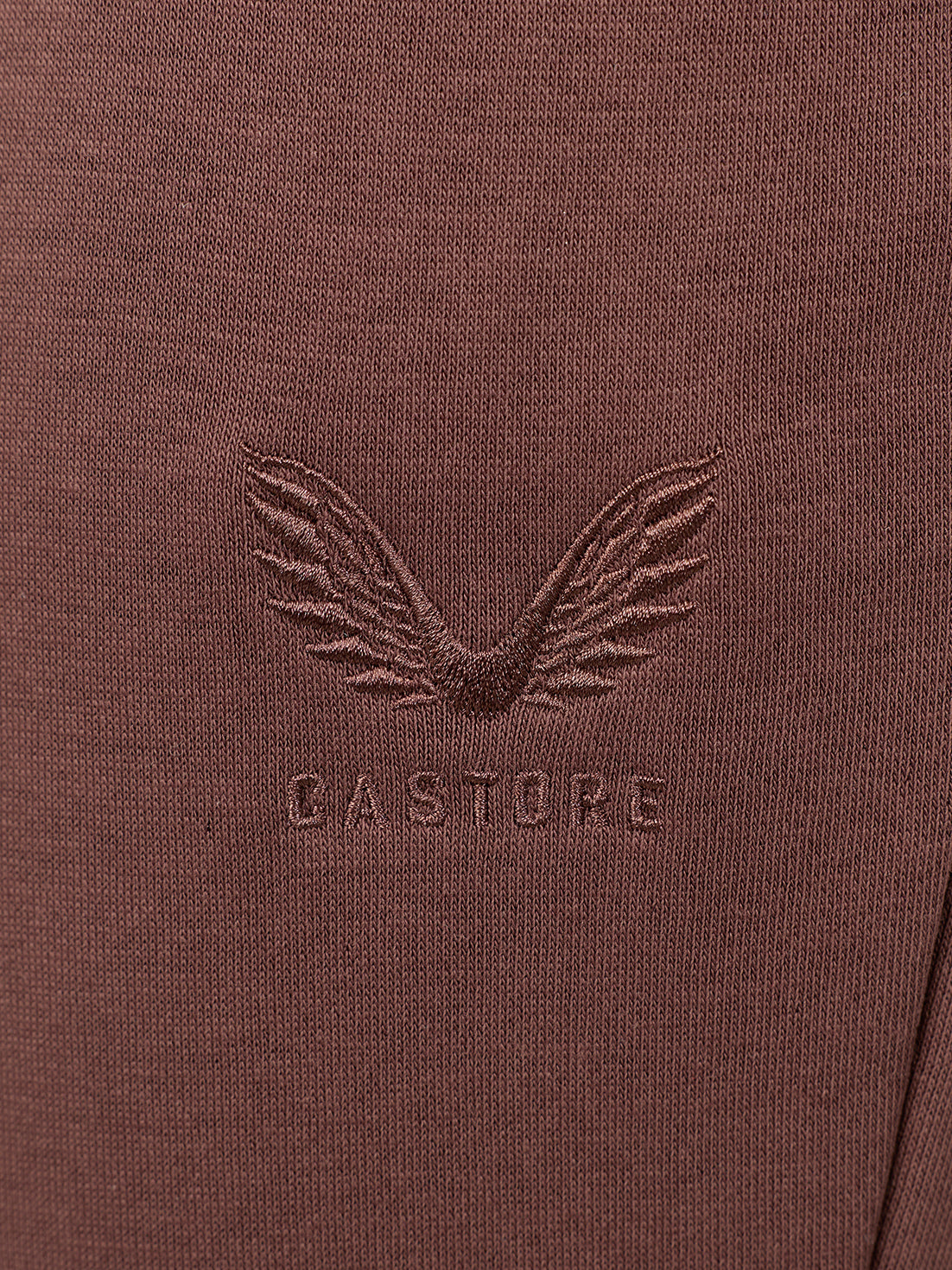 Close-up of a brown textured knit fabric with an embossed winged logo and the word 'CASTORE' centered on the chest.