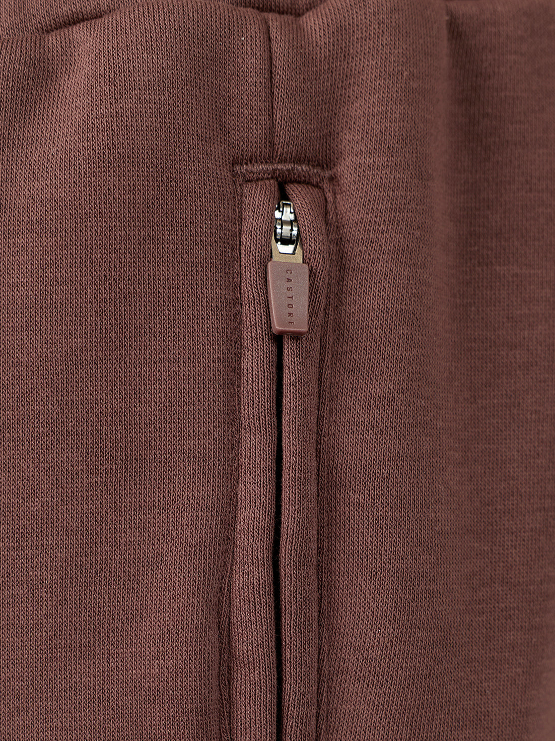 Close-up of a brown knit garment featuring a vertical zippered pocket with a matching brown pull tab.