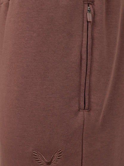 Close-up of a brown ribbed knit garment featuring a vertical zippered pocket and an embroidered winged logo near the bottom.
