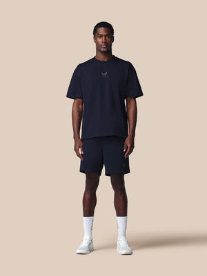 Man wearing a navy t-shirt and shorts set with white socks and shoes on a beige background