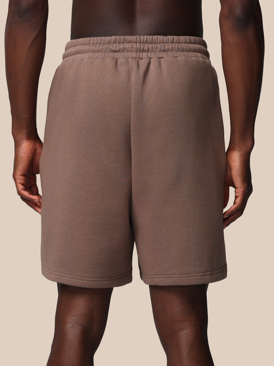 Brown sweat shorts worn by a person on a beige background