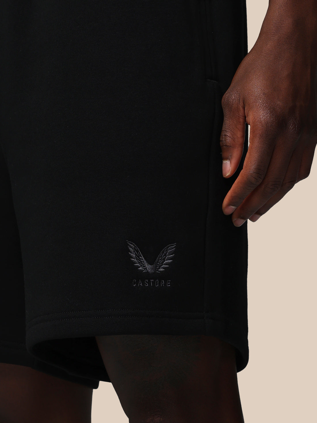 Black shorts with a logo on the waistband against a beige background